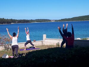 Bild zeigt Gruppe von 4 Menschen, die Yogaübungen am Strand machen.